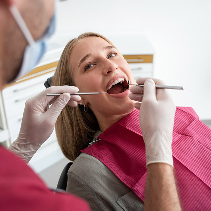 Zahnarzt mit Mundschutz kontrolliert Zähne einer Patientin auf Behandlungsstuhl. 