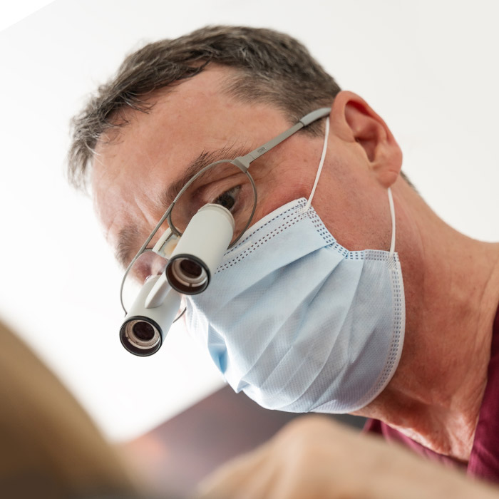 Dr. Krug mit Mundschutz und Lupenbrille während einer Behandlung